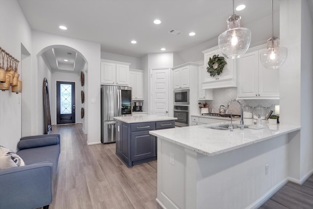 kitchen featuring arched walkways, white cabinetry, open floor plan, hanging light fixtures, and appliances with stainless steel finishes