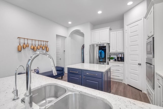 kitchen with light stone counters, a kitchen island, a sink, white cabinets, and appliances with stainless steel finishes