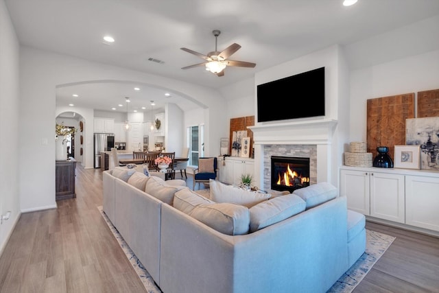 living area featuring visible vents, a ceiling fan, a stone fireplace, light wood-style floors, and recessed lighting