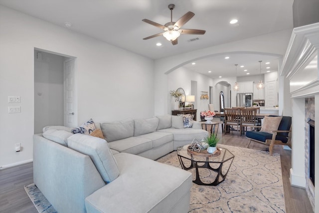 living room featuring arched walkways, a ceiling fan, wood finished floors, a fireplace, and recessed lighting