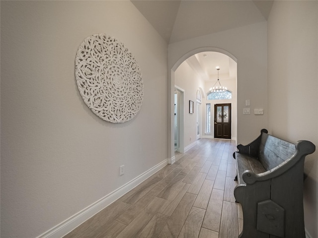 foyer with baseboards, wood finish floors, arched walkways, vaulted ceiling, and a notable chandelier