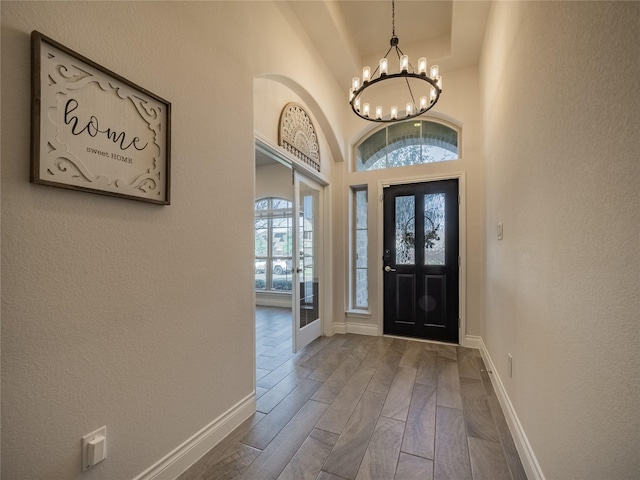 foyer entrance with baseboards, dark wood finished floors, a chandelier, french doors, and a high ceiling