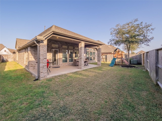 rear view of house featuring a patio, a fenced backyard, a playground, a yard, and brick siding