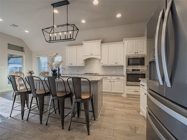 kitchen featuring tasteful backsplash, light stone countertops, a kitchen bar, appliances with stainless steel finishes, and white cabinetry