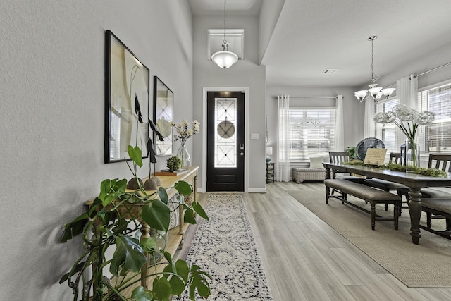 entryway featuring a healthy amount of sunlight, light wood finished floors, baseboards, and a notable chandelier