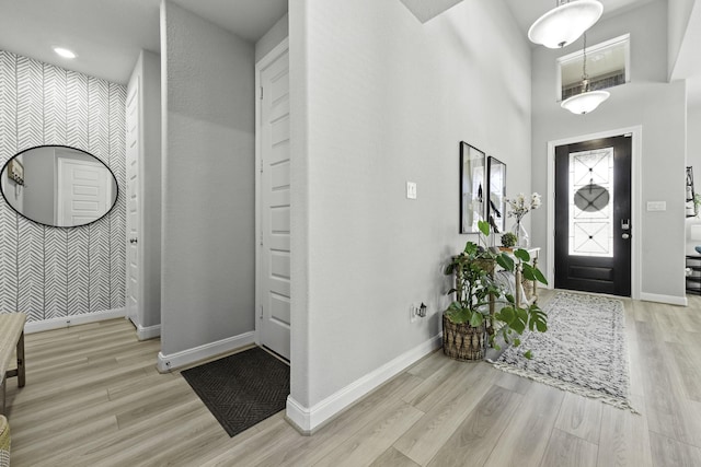 entryway with an accent wall, light wood-style floors, a towering ceiling, and baseboards