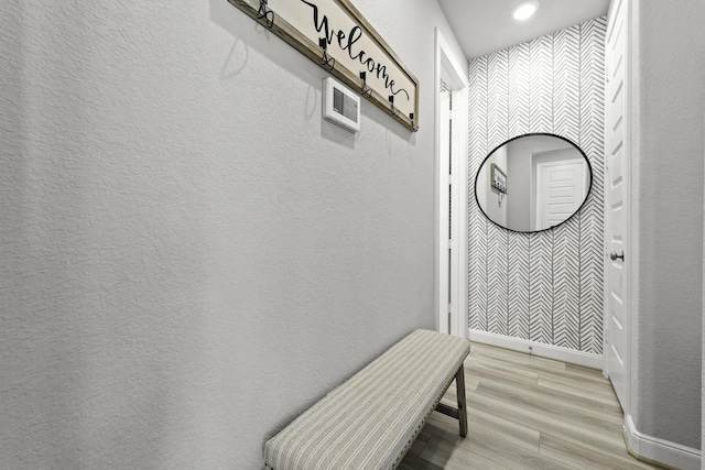 interior space featuring light wood-type flooring, a textured wall, and baseboards