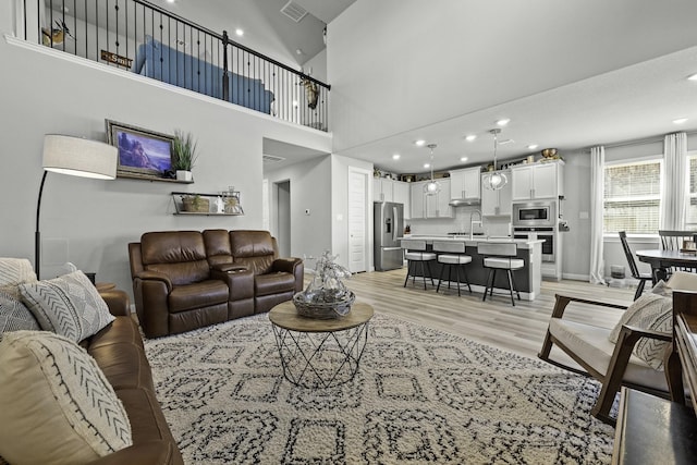 living area featuring visible vents, baseboards, a towering ceiling, light wood-style flooring, and recessed lighting