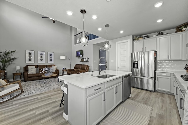 kitchen featuring an island with sink, open floor plan, stainless steel appliances, light countertops, and a sink