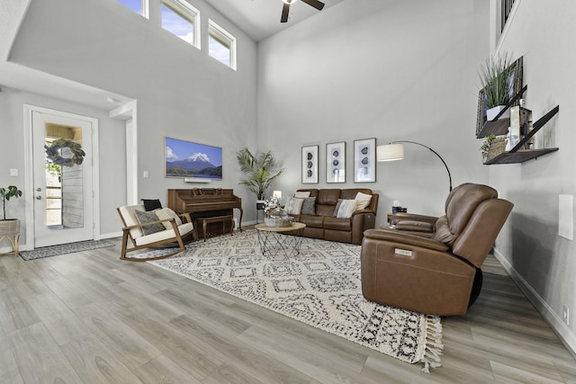 living area featuring baseboards, a high ceiling, a ceiling fan, and light wood-style floors