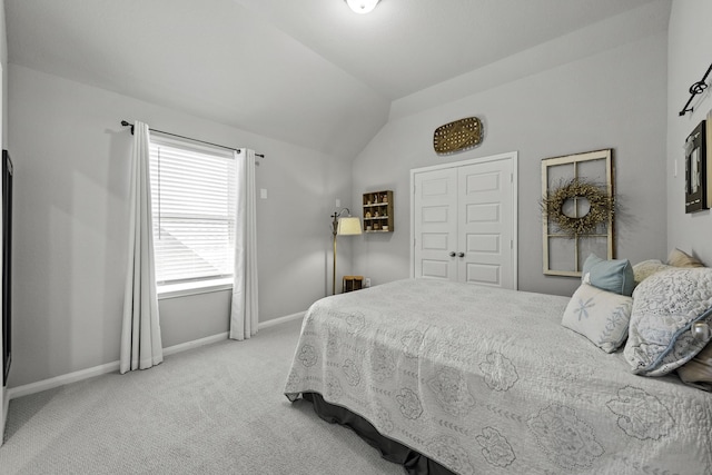 bedroom with a closet, light colored carpet, vaulted ceiling, and baseboards