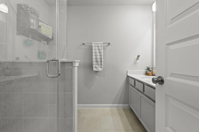 bathroom with vanity, baseboards, tiled shower, and tile patterned floors