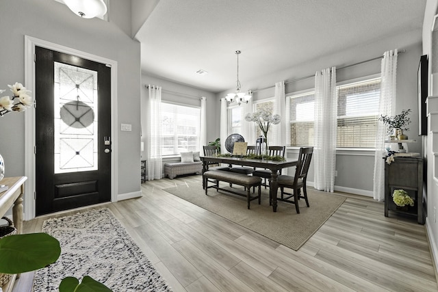 dining area with baseboards, light wood-type flooring, visible vents, and an inviting chandelier