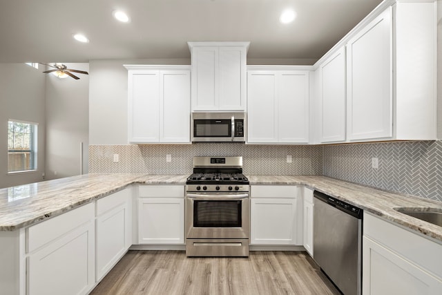 kitchen with appliances with stainless steel finishes, white cabinets, light wood-style floors, and a peninsula