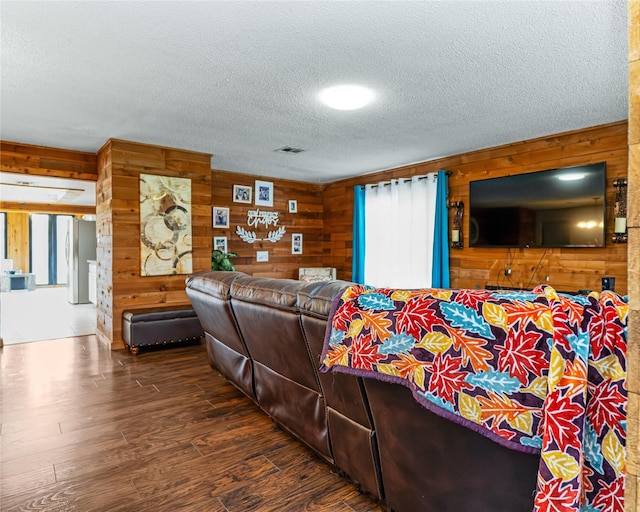 living area featuring visible vents, dark wood finished floors, wood walls, and a textured ceiling