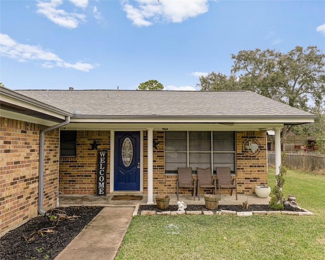 view of exterior entry featuring brick siding, a yard, and roof with shingles