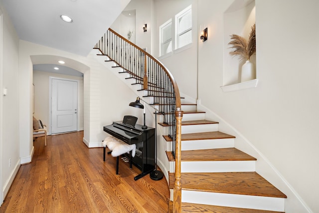 staircase featuring baseboards, arched walkways, wood finished floors, and recessed lighting