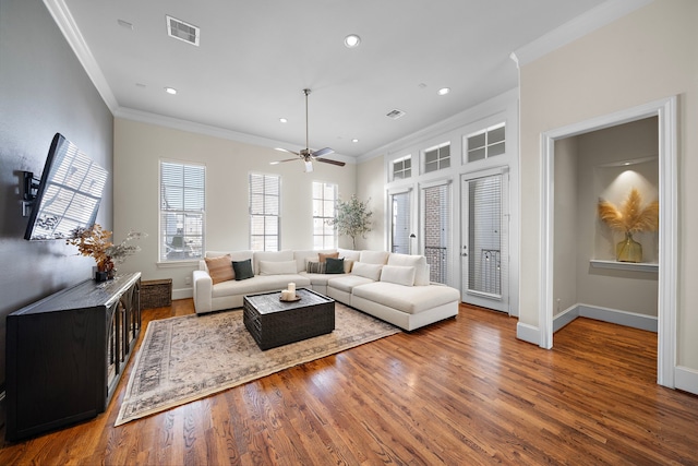 living area with ornamental molding, wood finished floors, visible vents, and baseboards