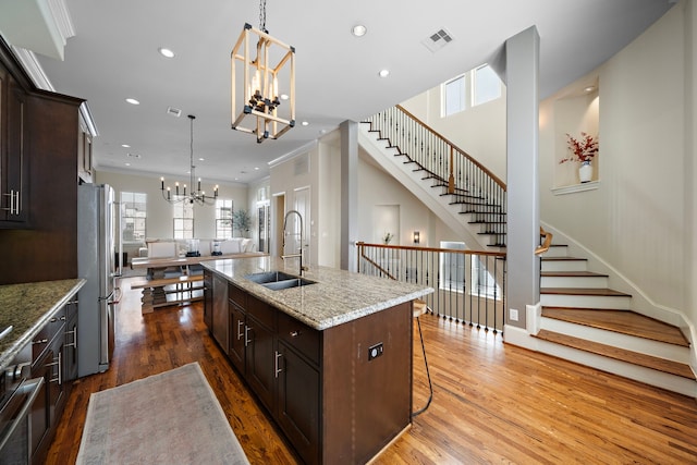 kitchen featuring dark brown cabinetry, a center island with sink, appliances with stainless steel finishes, an inviting chandelier, and a sink