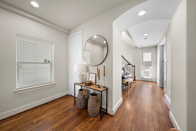 hallway featuring arched walkways, dark wood finished floors, stairs, and baseboards