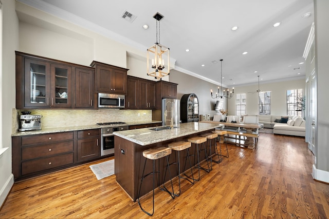 kitchen with stainless steel appliances, an inviting chandelier, glass insert cabinets, open floor plan, and a kitchen bar