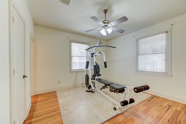 workout area with ornamental molding, light wood-type flooring, visible vents, and baseboards