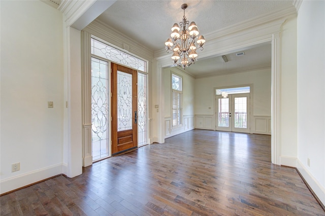 entryway featuring french doors, crown molding, a decorative wall, dark wood-type flooring, and a chandelier