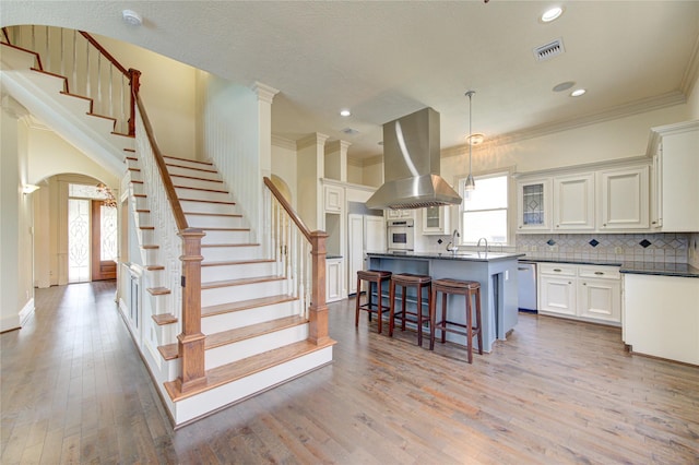 kitchen featuring visible vents, dark countertops, light wood-style flooring, a kitchen breakfast bar, and island exhaust hood