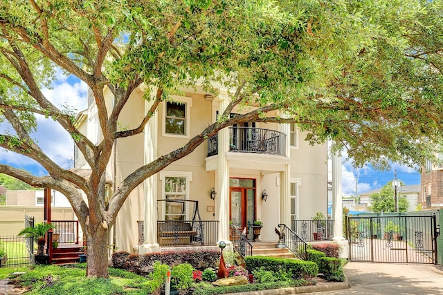 view of front of home featuring a gate, fence, a balcony, and stucco siding