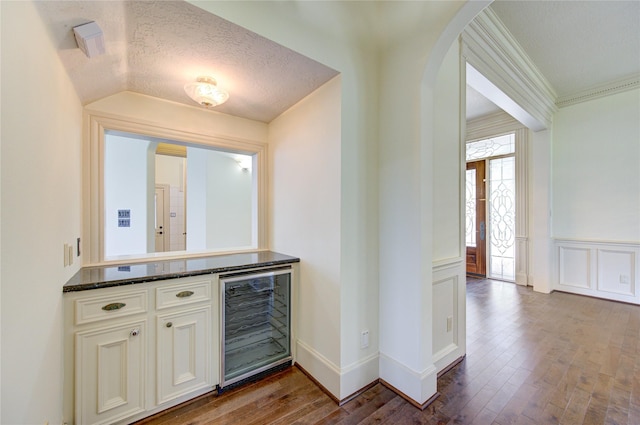 bar with a textured ceiling, wine cooler, arched walkways, and dark wood-type flooring