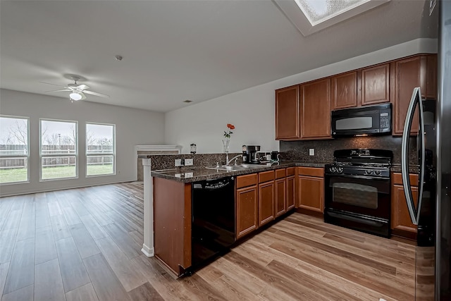 kitchen with a skylight, brown cabinets, light wood-style flooring, a peninsula, and black appliances