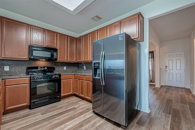 kitchen with a skylight, visible vents, decorative backsplash, light wood-style floors, and black appliances