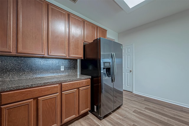 kitchen with a skylight, brown cabinetry, light wood-style floors, refrigerator with ice dispenser, and backsplash