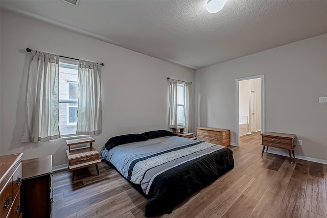 bedroom with light wood-style flooring, baseboards, and a textured ceiling