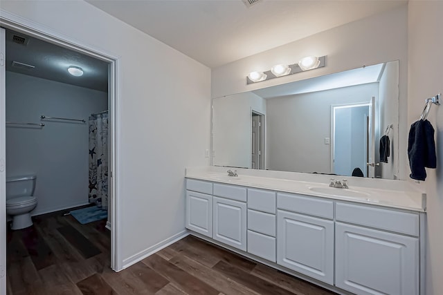 bathroom featuring double vanity, a sink, toilet, and wood finished floors