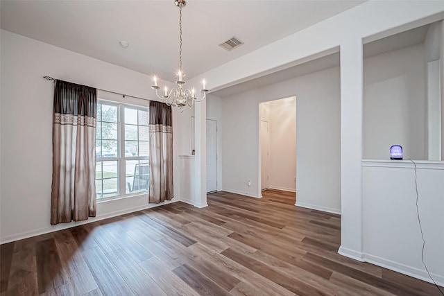 unfurnished dining area featuring baseboards, visible vents, a chandelier, and wood finished floors