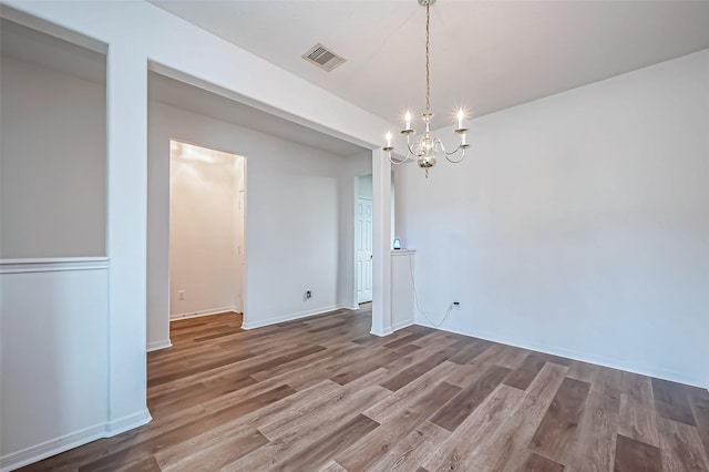 unfurnished dining area featuring baseboards, visible vents, an inviting chandelier, and wood finished floors