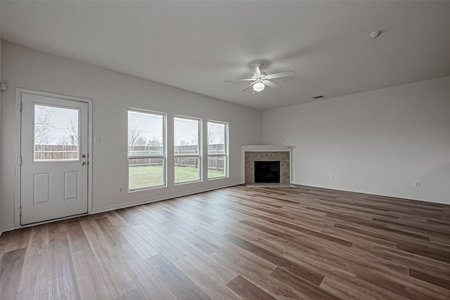 unfurnished living room with a high end fireplace, visible vents, ceiling fan, and wood finished floors