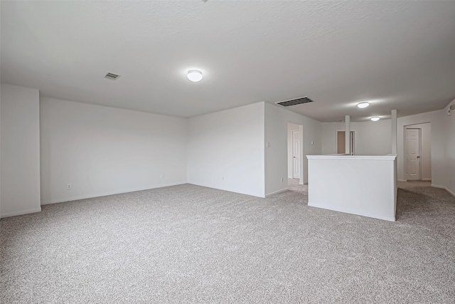 spare room featuring light carpet, visible vents, and a textured ceiling