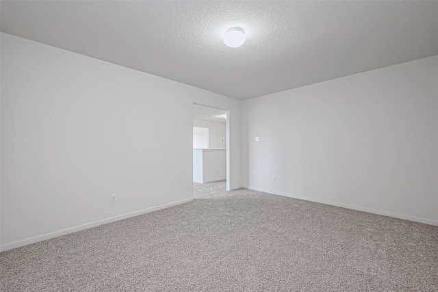 empty room with light carpet, a textured ceiling, and baseboards