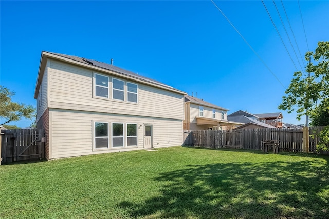 back of house with a lawn, a fenced backyard, a gate, and roof mounted solar panels