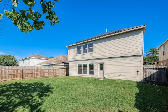 rear view of property featuring a fenced backyard, a lawn, and solar panels