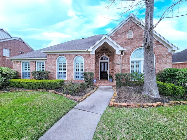 view of front of house with brick siding, a front lawn, and a shingled roof