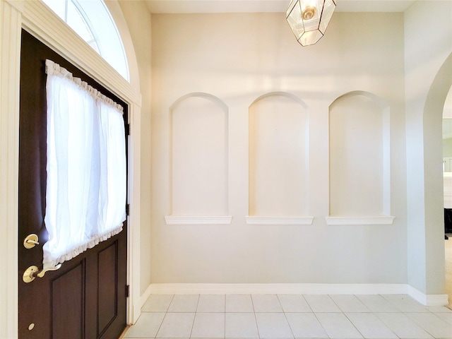 foyer with light tile patterned floors, arched walkways, and baseboards