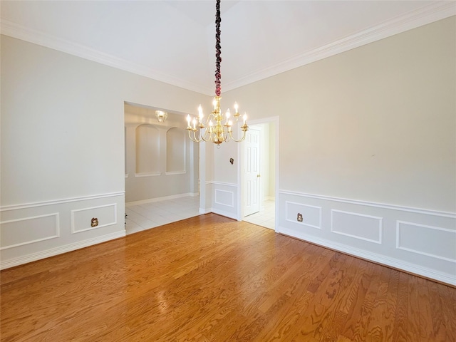 unfurnished dining area featuring crown molding, an inviting chandelier, wainscoting, light wood finished floors, and a decorative wall