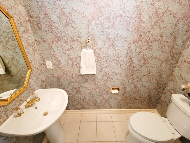 half bath featuring a sink, tile patterned floors, baseboards, toilet, and wallpapered walls