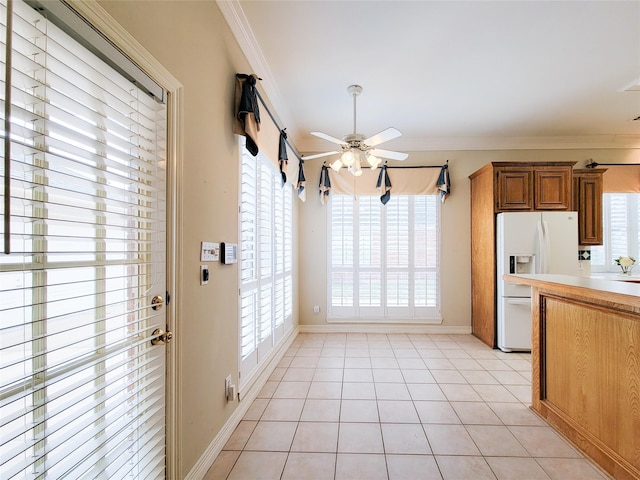 kitchen with plenty of natural light, ceiling fan, white refrigerator with ice dispenser, ornamental molding, and light tile patterned flooring