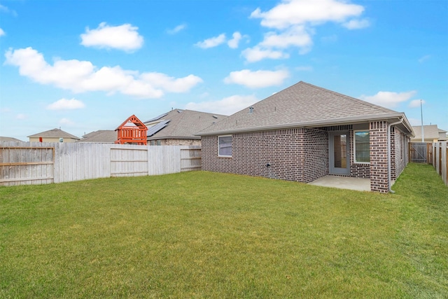 rear view of property featuring a lawn, a patio, a fenced backyard, roof with shingles, and brick siding