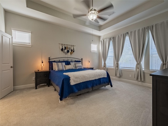 bedroom with baseboards, a tray ceiling, multiple windows, and light colored carpet