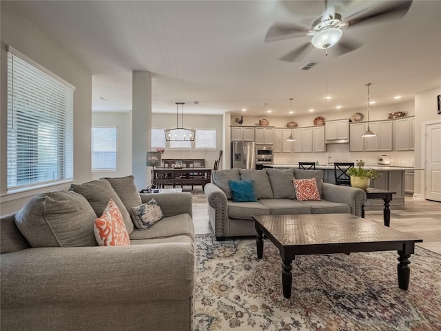 living area with light wood-style flooring, visible vents, and ceiling fan with notable chandelier